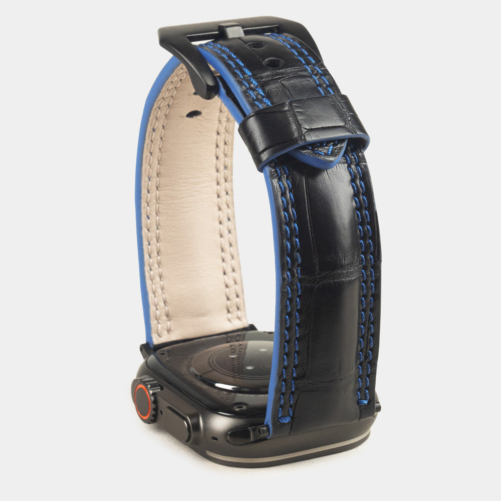 Apple Watch Ultra 49 mm aus schwarzem Alligatorleder, Naht und Kante in Blau, mit schwarzen Adaptern und Schnalle | Gehäuse unten, um die blau gefärbte Kante zu sehen