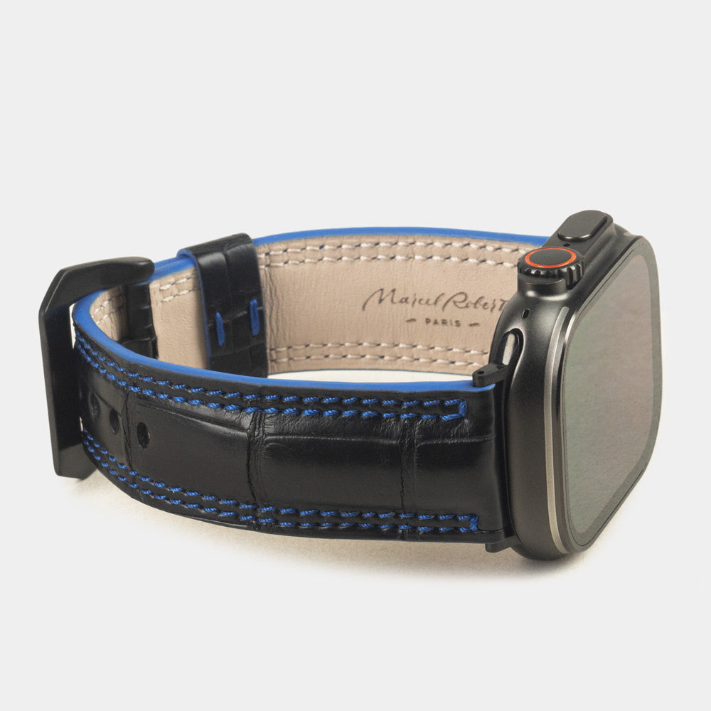 Apple Watch Ultra 49 mm aus schwarzem Alligatorleder, Naht und Kante in Blau, mit schwarzen Adaptern und Schnalle | 3/4-Ansicht mit Innenfutter aus Leder und Marcel-Robert-Signatur