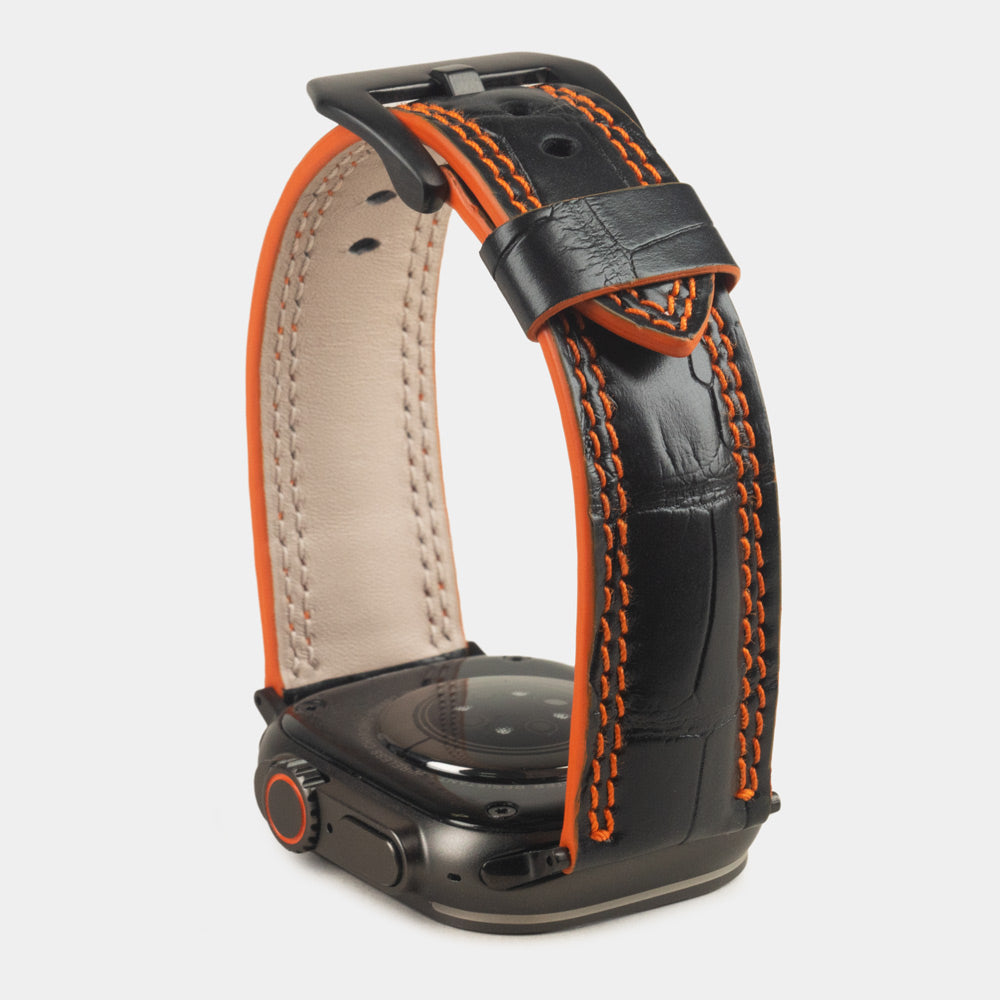 Apple Watch Ultra 49 mm aus schwarzem Alligatorleder, Naht und Kante in Orange, mit schwarzen Adaptern und Schnalle | Gehäuse unten, um die orange gefärbte Kante zu sehen